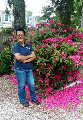 Smiling Woman standing outside next to fuscia rhododendron tree