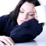 Woman in navy robe with her eyes closed holding a white coffee cup