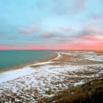 Beautiful view of Cape Code Beach in the winter time with snow on the shore, turquoise water and pink and white sky